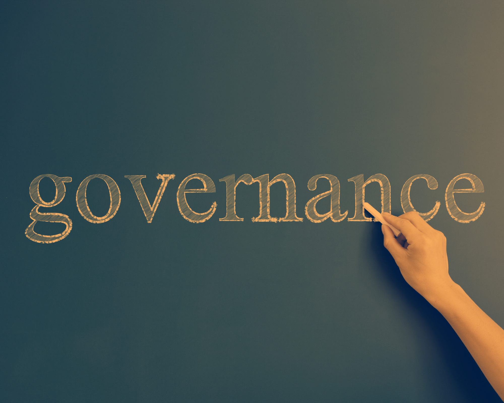 The word governance is written on a chalk board with a hand holding chalk pointing to the word